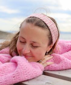 a woman laying on top of a wooden bench wearing a pink sweater and headband