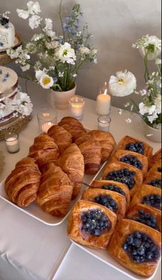 there are many pastries on the table with candles and flowers in vases behind them