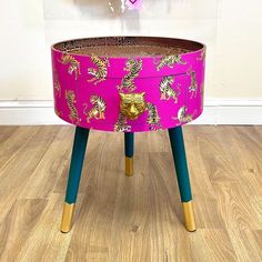 a pink and gold painted table with legs on wood flooring next to white wall