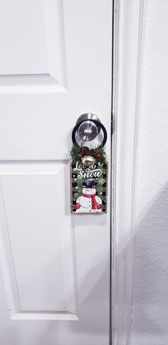 This charming door decor is a fantastic way to help bring that feeling of Christmas into your entryway, your home or office. This Door Charm is attached to a lovely sign with a cheerful snowman that says "Let It Snow. "  The handle is wrapped with black ribbon. It is embellished with a gold bell, pine shrubs, pine cones and berries, on a green and black plaid  background.  This decor will be perfect for door knob decorations. This will make a perfect addition to your holiday decorations. Comes f Christmas Door Knob Hangers, Snowman Door Knob Hanger Sayings, Snowman Door, Let It Snow, Black Ribbon, Door Knobs, Pine Cones, Door Hangers, Door Wreaths