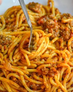 someone is eating spaghetti with meat sauce in a white bowl and holding a fork up to it