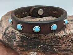 a brown leather bracelet with turquoise stones on top of it, sitting on a rock