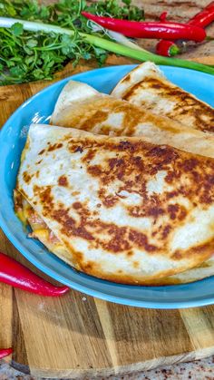 three quesadillas on a blue plate with red chili peppers and parsley