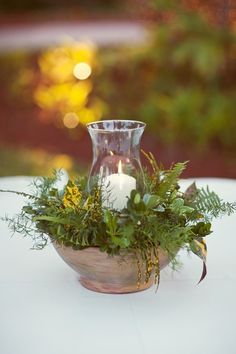 a vase filled with greenery sitting on top of a white table covered in candles