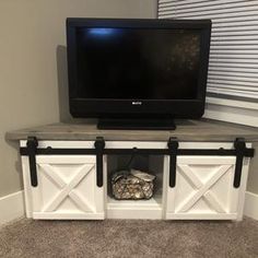 a flat screen tv sitting on top of a wooden entertainment center next to a window