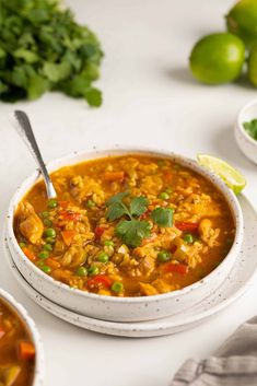 a white bowl filled with soup next to limes and cilantro on a table