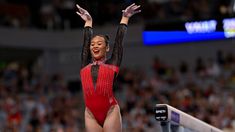 a woman in a red and black leotard is standing on a balance beam