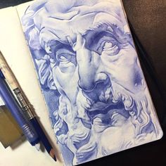 a drawing of a man's face on top of a book next to a pen