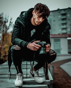 a man sitting on top of a metal bench holding a camera next to his legs