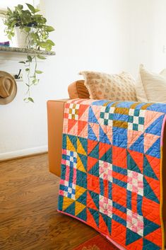 a couch with a colorful quilt on top of it next to a potted plant