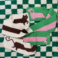 three knitted sweaters laying on top of a green and white checkered blanket