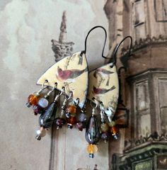 The Naomi Earrings, made on Father's Day and named for a paternal ancestor, feature enameled copper charms by TendancePerles depicting birds. Though different, each image is compatible in theme and color. The charms support dangles on silver head pins of Czech glass, carnelian, green garnet, Botswana agate and golden pyrite. Measuring about 2 inches from where earring attaches to wire, they are on silver ear wires by metamorphSupplies.  Weight (each) is .2 ounce or 7 grams. Copper Dangle Earrings With Patina, Copper Bird Earrings, Bohemian Multi-stone Dangle Jewelry, Green Bohemian Patina Earrings, Brown Patina Dangle Earrings, Botswana Agate, Green Garnet, Enameled Copper, Head Pins