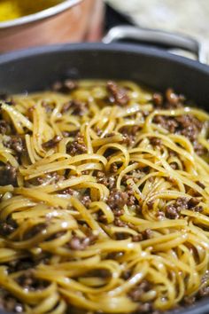 a pan filled with spaghetti and meat on top of a stove next to other cooking utensils