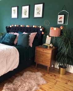 a bedroom with green walls, pink and white pillows and pictures on the wall above the bed