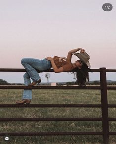 a woman leaning against a fence with her legs up on the rail and wearing a cowboy hat