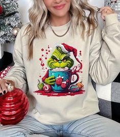 Indulge in the festive fun with this 'Giggling Grinch' unisex fleece sweatshirt! This merry piece is perfect for celebrating Grinchmas, showcasing a vibrant graphic of the iconic character enjoying a hot holiday treat. Made from a snug 50% cotton and 50% polyester mix, it promises warmth and softness for the chilly holiday season. This unisex sweatshirt, originating from Nicaragua, provides a comfortable fit for all, making it an excellent choice for holiday gifting or for bringing some playful Sweatshirt Graphic, Plus Swimwear, Grinch Christmas, Fleece Sweatshirt, Casual Fit, Casual Fits, Orange And Purple, Jeans Dress, T Shirt Top