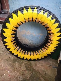 a yellow and black sunflower sitting on top of a cement ground next to a blue wall