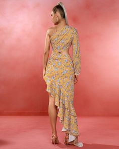 a woman in a yellow floral print dress and high heeled sandals standing on a pink background