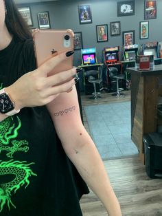 a woman with a dragon tattoo on her arm holding an iphone in a room full of video game machines