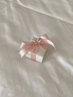 a white gift box with a pink bow on it sitting on top of a bed