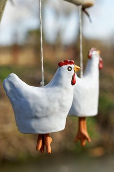 two white ceramic chickens hanging from a tree