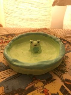 a green bowl with a frog in it on a bed