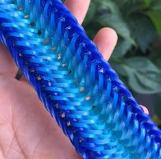 a hand holding a blue plastic object in it's left hand and green plants behind it