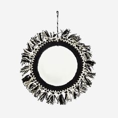 a round mirror with black and white fringes hanging from it's center point