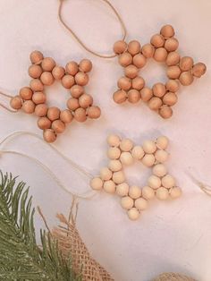 three wooden beads are hanging from twine strings next to pine cones on a white surface