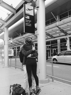 black and white photograph of two people hugging at an airport with cars in the background