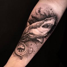 a man's arm with a shark and compass tattoo on it