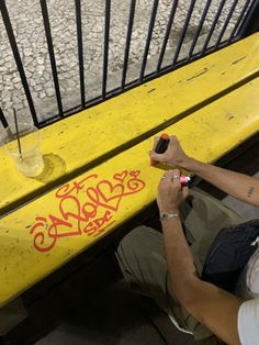 a man sitting on a yellow bench with graffiti writing on the side and holding a marker in his hand