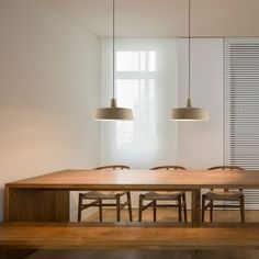 a wooden table with four chairs and two lamps hanging from it's sides in front of a window