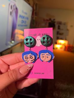 a person holding up two earrings with faces on them