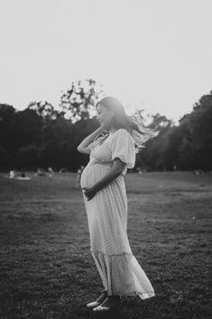 a pregnant woman standing in a field with her hair blowing in the wind, black and white photograph