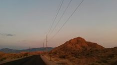 an empty road in the desert with power lines above it and mountains in the distance