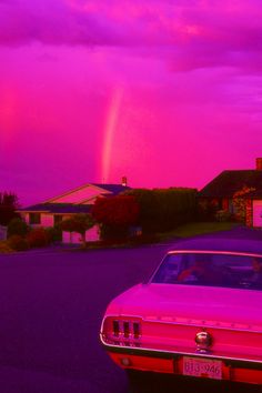 a pink car parked in front of a house under a purple sky with a rainbow