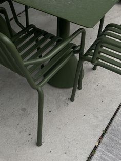 two green chairs sitting next to each other near a table and chair on the sidewalk