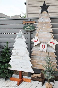 two wooden christmas trees sitting next to each other in front of a fence with signs on it