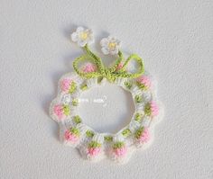 a crocheted wreath with pink and green flowers on it sitting on a white surface