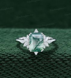 a green and white diamond ring on top of a green cloth with diamonds around it