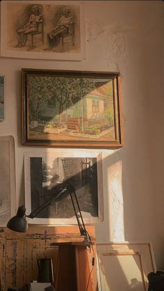 some pictures are hanging on the wall above a desk with a lamp and other items