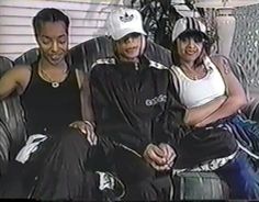 three people sitting on a couch with one person wearing a white hat and the other in black