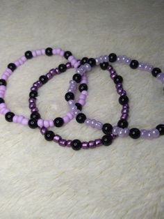 Perfect for a fan of purple!! Lots of purple!! Lightweight and super comfy, these are great for just a casual splash of color to any outfit. Made with glass beads (that's the purple) and plastic (that's the black), they're just cute and fun to have on! Each bracelet CAN vary in size due to the glass beads being variable sizes, but they measure approximately 18-19cms. They are made with .5mm elastic cord and just a little wee touch of jewelry glue to get that knot nice and SECURE! Because we can' Black And Purple Beaded Bracelets, Purple And Black Bracelet, Handmade Black Plastic Jewelry, Casual Purple Bracelets With Colorful Beads, Trendy Black Bracelets With Colorful Beads, Trendy Purple Beaded Bracelets, Adjustable Purple Bracelets With Black Beads, Adjustable Purple Bracelet With Black Beads, Purple Beaded Bracelets With Black Beads As A Gift