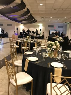 a room filled with tables and chairs covered in black table cloths, white plates and silverware