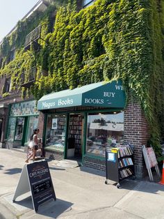 people are walking down the sidewalk in front of a book store with ivy growing up the side of it