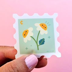 a person holding up a small stamp with flowers on it