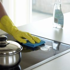 a person in yellow gloves cleaning a stove top with a blue cloth and sponge on it