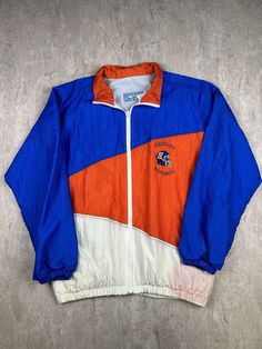 This vintage Hershey High School Trojans Football windbreaker jacket is a standout item for any high school football fan. In men's size 2XL, it features the Trojans' logo and colors, offering a stylish way to show school spirit while providing lightweight protection from the elements. Ideal for cool weather, this windbreaker combines functionality with a touch of nostalgia. Please refer to the provided pictures for a detailed view of the condition and measurements of this item. We strive to present our pieces as accurately as possible, ensuring you have a clear understanding of their fit and wear. We put in our best efforts to clean and remove any stains, marks, etc. from our vintage pieces, but due to the nature of these items, some imperfections may remain. If you have any questions or r Sporty Track Jacket For Sports Season Fan Gear, Casual Fan Gear Track Jacket For Sports Season, Casual Track Jacket For Sports Fans, Casual Track Jacket For Sports Season, Throwback Track Jacket For College Sports Season, Casual Team-colored Track Jacket For Fans, Retro Blue Windbreaker For College, Vintage Track Jacket For Sports Season, Vintage Track Jacket For Sports