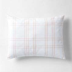 a white and pink plaid pillow on top of a white bedding with a light brown border